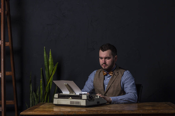 Bearded stylish writer typing on typewriter. Modern writer working on new book in office. Dark background. Space for text - Zdjęcie, obraz