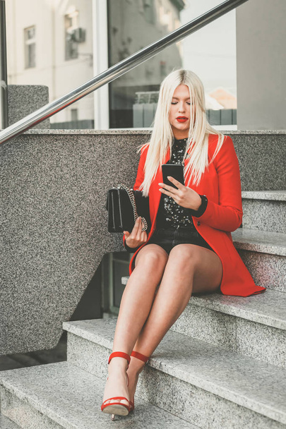 modische junge Frau sitzt draußen auf der Treppe und benutzt Handy - Bild - Foto, Bild