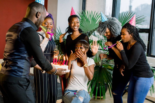 Portrait of charming African American girl blowing on candles on birthday cake surrounded by friends at party - Fotografie, Obrázek