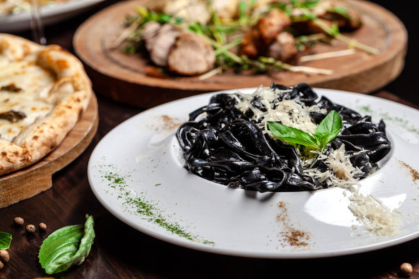The concept of Italian cuisine. Black pasta with cuttlefish ink, parmesan cheese and basil. Serving dishes in a restaurant in a white plate. copy space - Zdjęcie, obraz