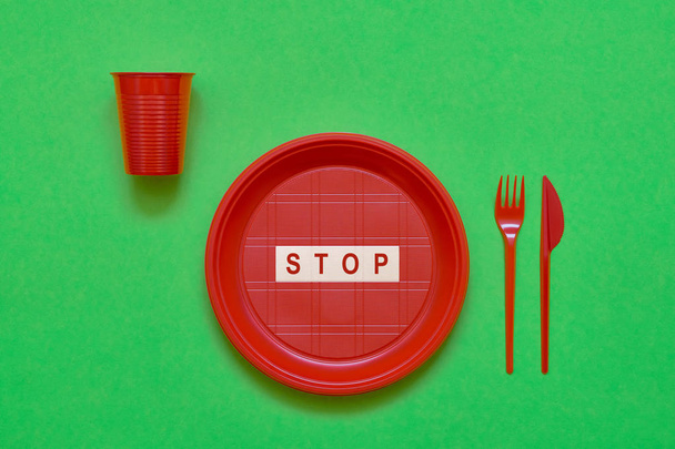 Disposable red plastic plate with word STOP inside, red knife and fork on green background. Top view, copy space. Plastic free concept. No Use symbol - Фото, зображення