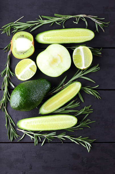 Green fruits, vegetables and rosemary on black boards with copy space. Avocado, lime, kiwi and green apple on wooden boards. Cucumbers and rosemary branches top view. Healthy food - Fotoğraf, Görsel