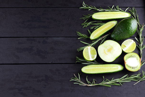 Green fruits, vegetables and rosemary on black boards with copy space. Avocado, lime, kiwi and green apple on wooden boards. Cucumbers and rosemary branches top view. Healthy food - Foto, imagen