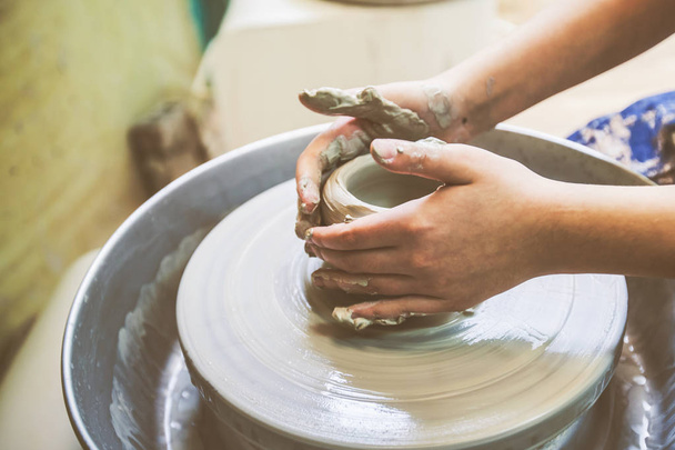 Manos de niño dando forma a la arcilla en la rueda de cerámica en el taller
. - Foto, Imagen