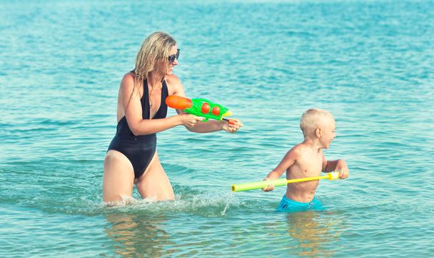 Mother and son play on the beach with water pistols. Summer time - Zdjęcie, obraz