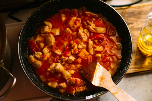 stir with a wooden spatula, cook. On the stove there is a frying pan with chicken in tomato sauce.Prepare a meal - Zdjęcie, obraz