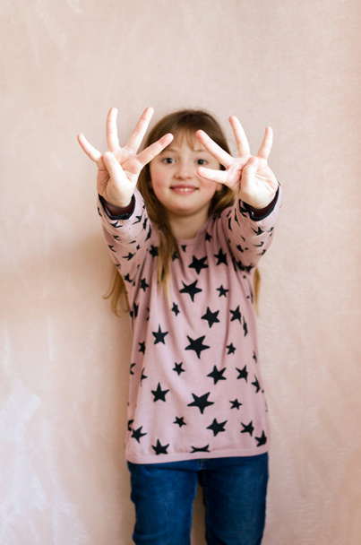 Little girl with long dark blonde hair and a cute smile on face showing 8 fingers like her age eight years. Focus on hands. Pink background. - Photo, Image