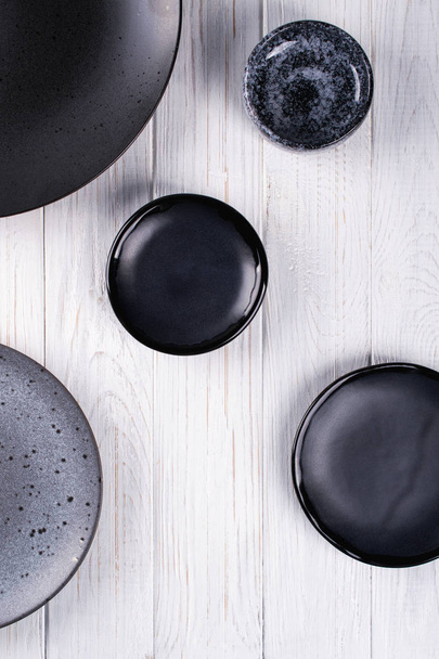 Ensemble de assiettes et bols gris et noirs en porcelaine sur une table en bois blanc. Pose plate
 - Photo, image