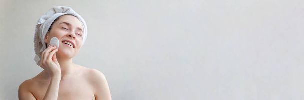 Portret van de schoonheid van lachende vrouw in handdoek op kop met een zachte gezonde huid make up verwijderen met wattenschijfje geïsoleerd op witte achtergrond. Huidverzorging reinigende spa relax concept. Banner - Foto, afbeelding