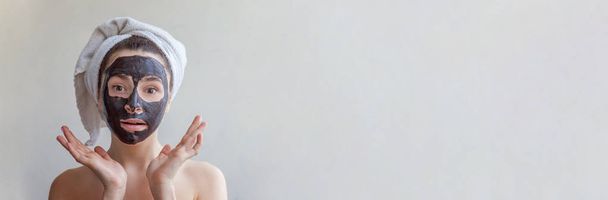 Απομονωμένη ομορφιά πορτρέτο γυναίκας σε πετσέτα στο κεφάλι εφαρμόζοντας μαύρο θρεπτική μάσκα στο πρόσωπο, λευκό φόντο. Περιποίηση καθαρισμού eco βιολογικά καλλυντικά spa Χαλαρώστε έννοια Banner - Φωτογραφία, εικόνα