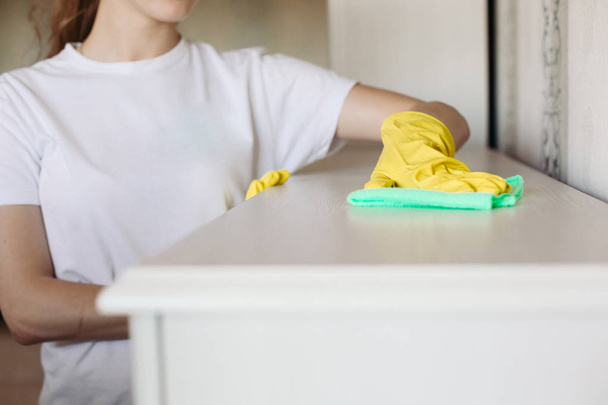 Cultivo de niña usando guantes de goma protectora amarilla, limpiando muebles
. - Foto, Imagen