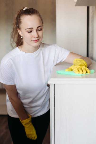 特別なミントの威嚇で家具を拭いて黄色いゴム手袋の身に着けている若い女の子. - 写真・画像