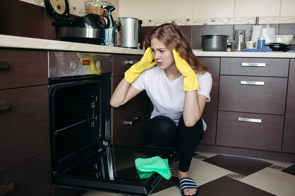 Donna in guanti protettivi gialli guardando forno sporco a casa cucina
. - Foto, immagini