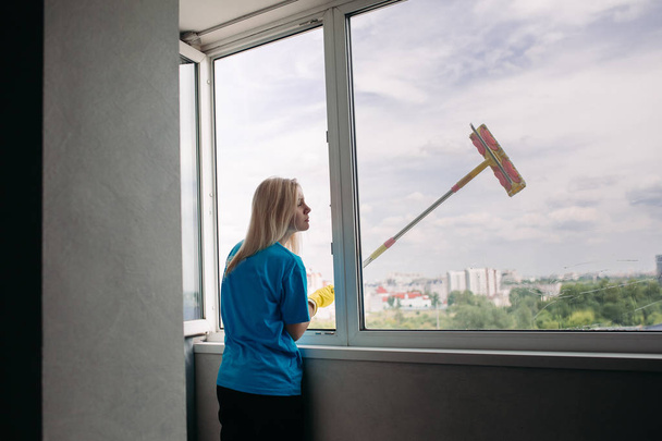Vue de jeune fille blonde nettoyant grande fenêtre ouverte
. - Photo, image