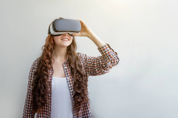 白い背景にVRメガネヘルメットヘッドセットを使用して身に着けている笑顔の若い女性。仮想現実ゴーグルを使用してスマートフォン。技術、シミュレーション、ハイテク、ビデオゲームの概念 - 写真・画像