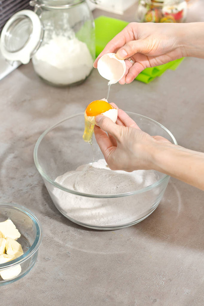 Female hands while breaking the chicken egg. Separation of the yolk from the protein. Adding an egg to the ingredients prepared to bake cakes. - Photo, image