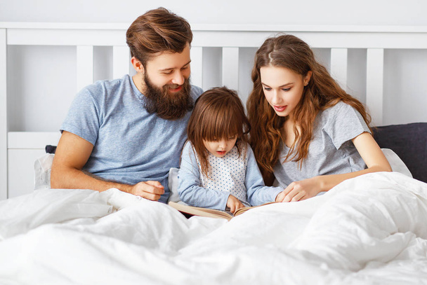 happy family mother, father and  father child daughter read a book, a fairy tale in be - Fotografie, Obrázek