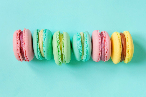 Sweet almond colorful pink blue yellow green macaron or macaroon dessert cake isolated on trendy blue pastel background. French sweet cookie. Minimal food bakery concept. Flat lay top view copy space - Photo, Image