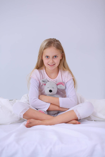 La niña en el dormitorio está sentada en la cama. La niña está usando un pijama y sentada en la cama
 . - Foto, imagen
