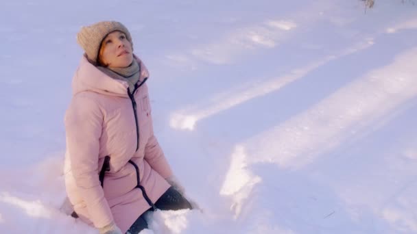 きれいな雪の滑らかで見て白に囲まれた雪の吹きだまりに座っているアクティブな若い女性 - 映像、動画