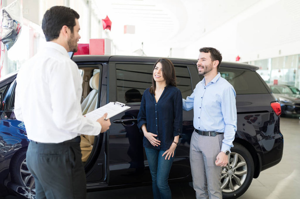 Πωλητής συζητώντας χαρακτηριστικά αυτοκινήτων με τους πελάτες στην αντιπροσωπεία - Φωτογραφία, εικόνα