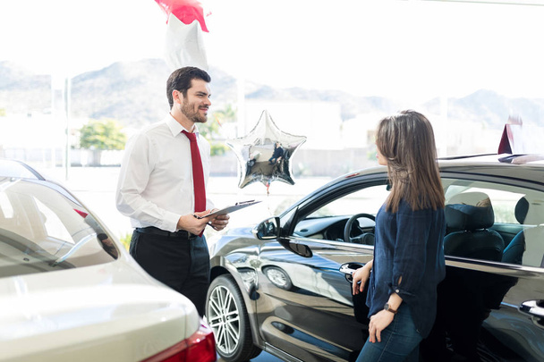 Attractive salesman giving information to woman about expensive car at salon - Photo, Image