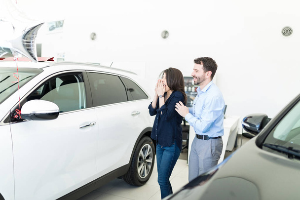 Μέσα του ενήλικα άνθρωπο έκπληξη γυναίκα με νέο αυτοκίνητο για τα γενέθλιά της στο σαλόνι αντιπροσωπεία αυτοκινήτων - Φωτογραφία, εικόνα