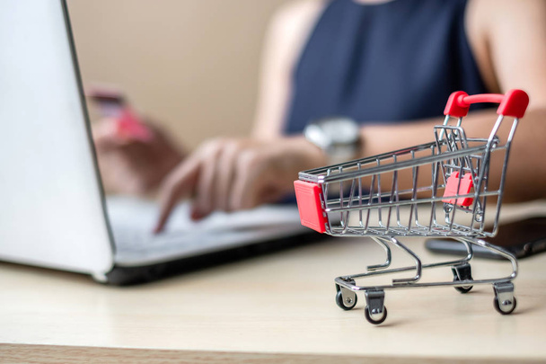 close up mini cart, Asian businesswoman holding credit card and using laptop for online shopping while making orders. internet, technology, ecommerce and online payment concept - 写真・画像