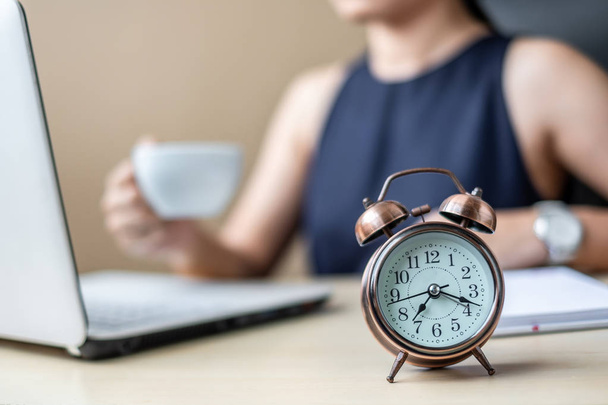 Закройте будильник с молодой бизнес-леди, используя маркетинговый план анализа ноутбука и пить кофе утром. Бизнес, финансы и образ жизни
 - Фото, изображение