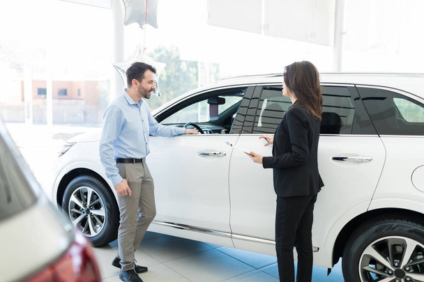 Zvědavý polovina dospělých klientů při pohledu na nový model automobilu zároveň prodavačka vysvětlí v showroomu - Fotografie, Obrázek