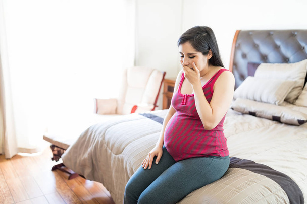 Žena během poslední fáze těhotenství pocit vomitish, zatímco sedí na posteli - Fotografie, Obrázek