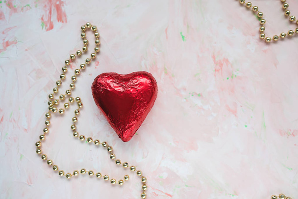 Çikolata kalp kırmızı folyo ve pembe bir arka plan üzerinde altın dekoratif boncuk. Sevgililer günü kavramı, copyspase. - Fotoğraf, Görsel
