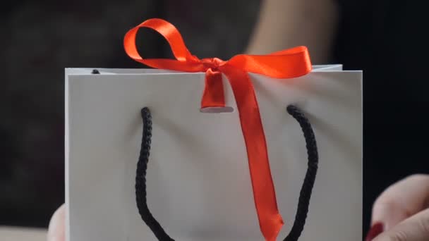 Κοντινό πλάνο γυναικεία δάχτυλα δείχνει κουτί δώρου χαρτί με κόκκινη κορδέλα και φιόγκο. ανοίγοντας ένα δώρο που κρατά το gift box ως γυναίκα λύνει το τόξο κόμπο πάνω σε μαύρο φόντο. HD - Πλάνα, βίντεο