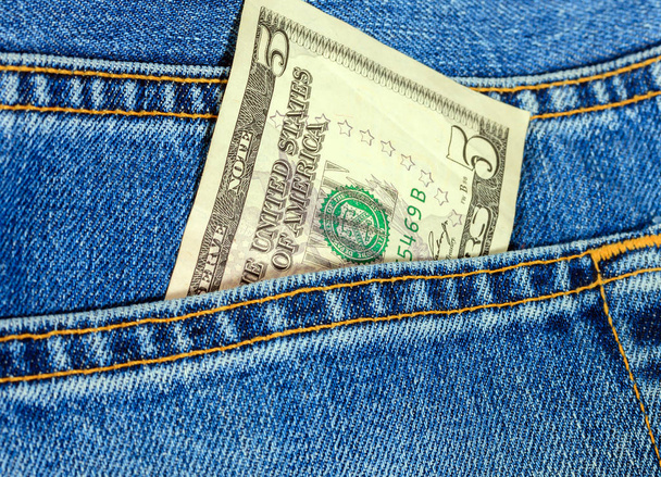 5 dollar bill ons uit een blauwe jean zak uit. Amerikaanse dollar biljetten op blauwe denim jeans achtergrond. Dollar Amerikaans geld cash. - Foto, afbeelding