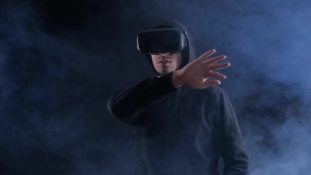 Hombre con capucha usando auriculares de realidad virtual en fondo ahumado negro
. - Imágenes, Vídeo