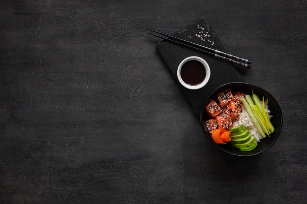 Colorful Asian trendy food, sushi poke bowl with rise, cucumber, salmon, carrot, avocado, Sesame Seeds and soy sauce. Top view, close up - Foto, Imagem