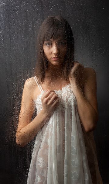 The brunette in a white dress for a wet glass on a black background. - Foto, afbeelding