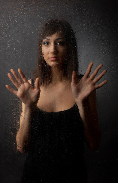 The brunette in a black dress for a wet glass on a black background. - Zdjęcie, obraz