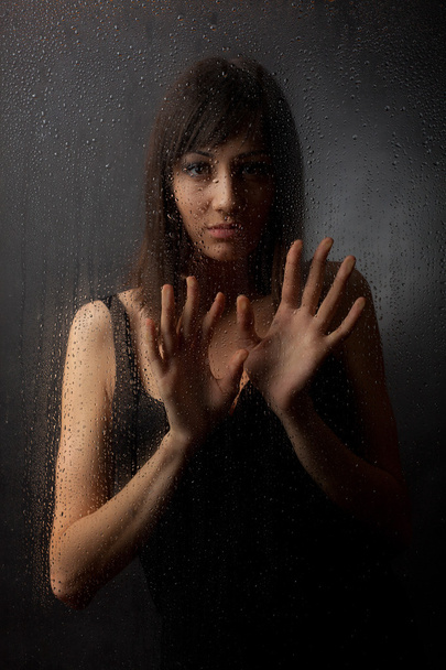 The brunette in a black dress for a wet glass on a black background. - Valokuva, kuva