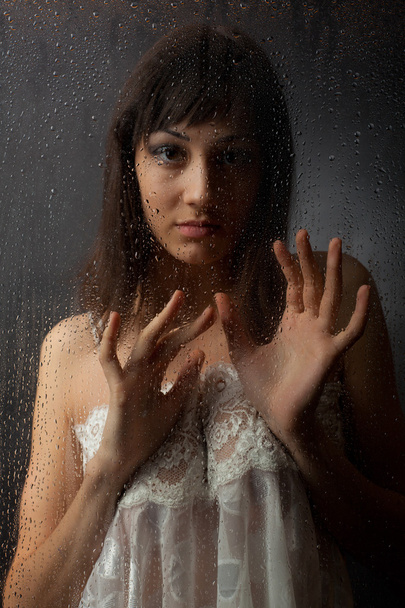 The brunette in a white dress for a wet glass on a black background. - Photo, image