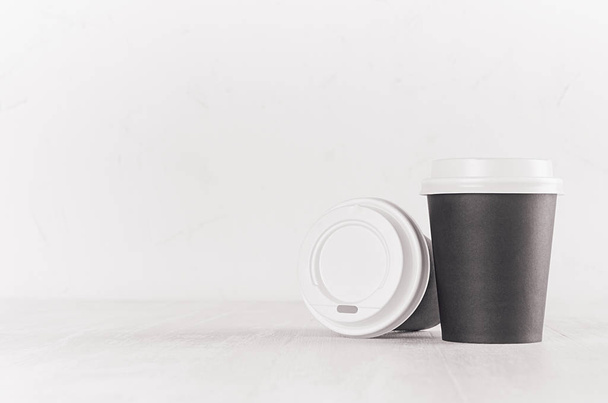Kaffee-Attrappe - schwarze Pappbecher und leere weiße Kappe auf weißem Holztisch mit Kopierraum, Café-Interieur. modernes elegantes Konzept für Markenidentität, Werbung, Design. - Foto, Bild