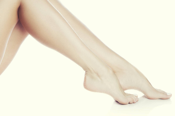 Μερική άποψη του γυναικεία πόδια με λευκό μανικιούρ σε άσπρο φόντο - Φωτογραφία, εικόνα