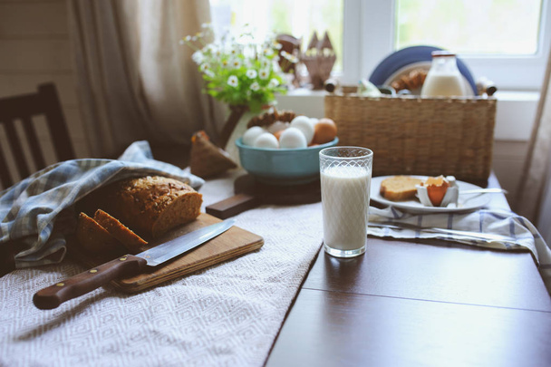 country breakfast on rustic home kitchen with farm eggs, butter, wholegrain bread and milk. Organic homemade food, easter concept.   - Фото, изображение