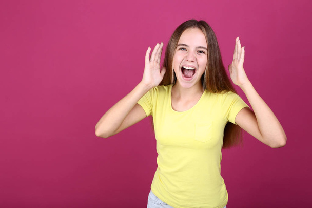 Young screaming girl in yellow t-shirt on pink background - Photo, Image