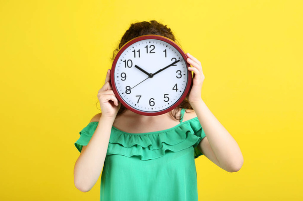 Young girl holding clock on yellow background - Zdjęcie, obraz