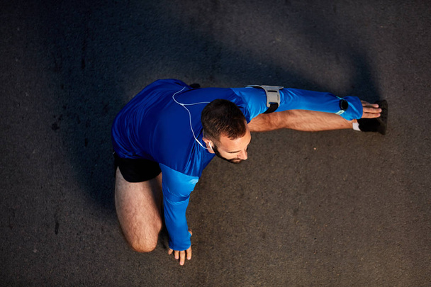 Bovenaanzicht voor knappe Kaukasische mannelijke runner benen strekken op straat. - Foto, afbeelding