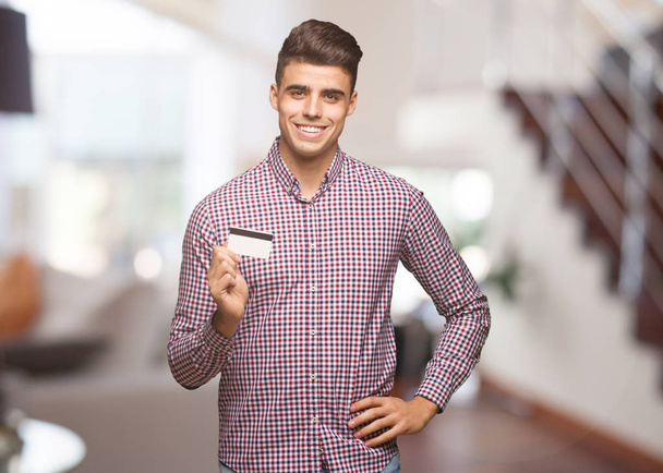 Νεαρός άνδρας κρατά πιστωτική κάρτα με τα χέρια στους γοφούς - Φωτογραφία, εικόνα