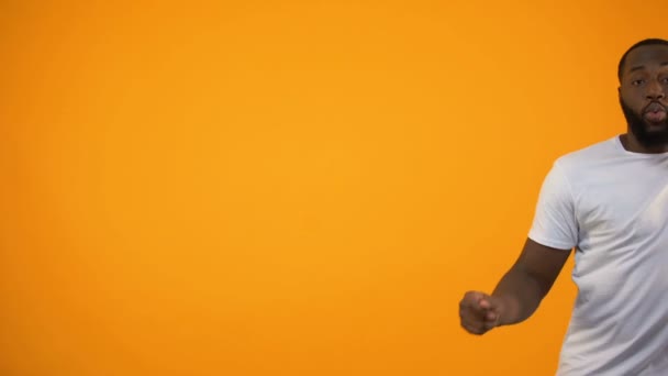 Afro-American man dancing against yellow background, feeling rhythm of music - Imágenes, Vídeo