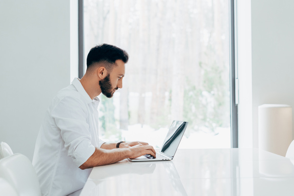 Brunette man geconcentreerd in wit overhemd laptop toetsenbord - Foto, afbeelding
