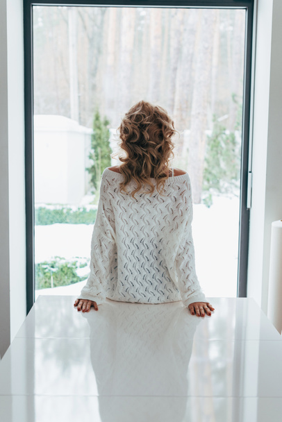 Back view of curly woman in knitted sweater looking at window - Φωτογραφία, εικόνα